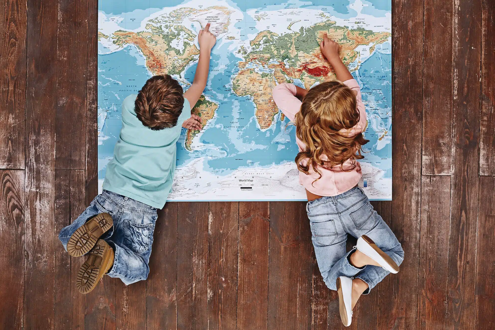 Discover the World. Children lying on world map, looking at it