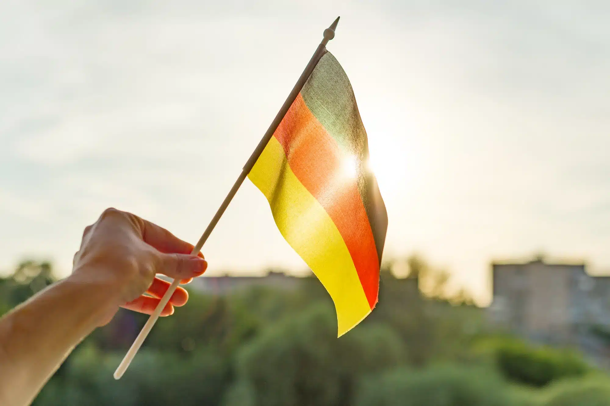 Hand holding Germany flag an open window. Background blue sky, silhouette of the city, sunset