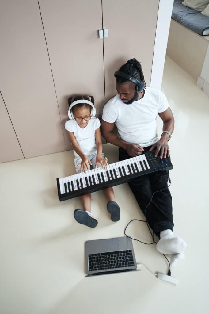 Adult African American father next to daughter plays the synthesizer