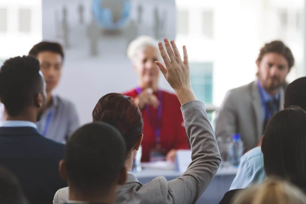 Businesswoman raising hand while woman allowed her to speak at business seminar in office building