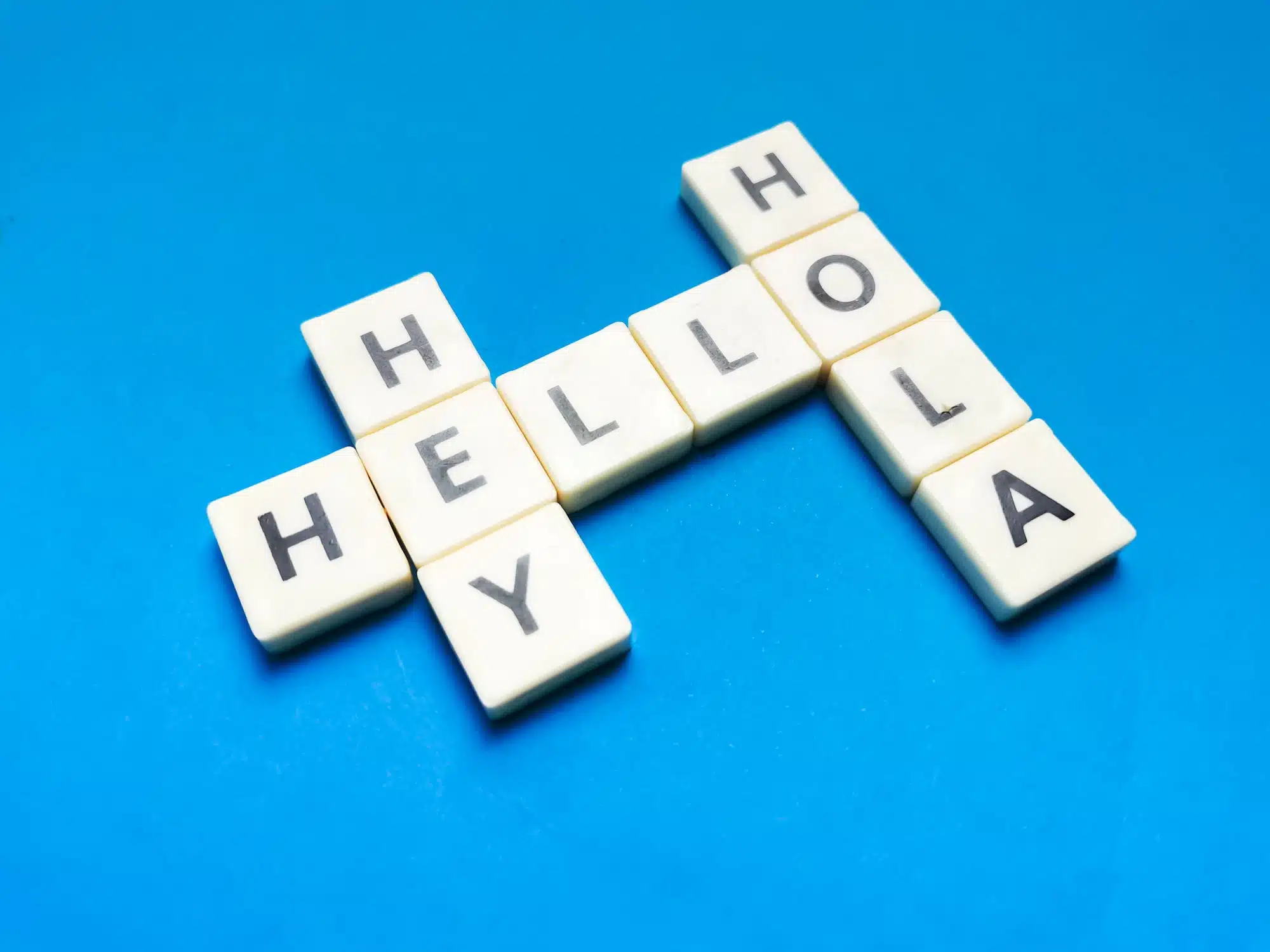 Hey Hola Hello made of square letter tiles against blue background.