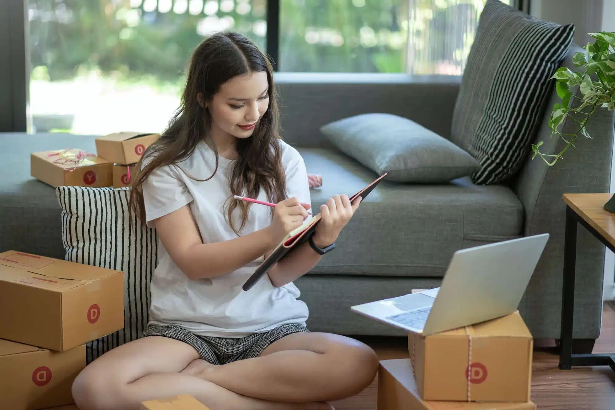 Young Asian businesswoman sell thing online, preparing boxes and taking notes for customer at home.
