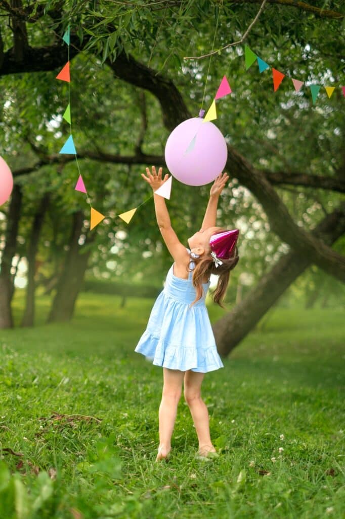 Girl plays with festive decor in garden on birthday.
