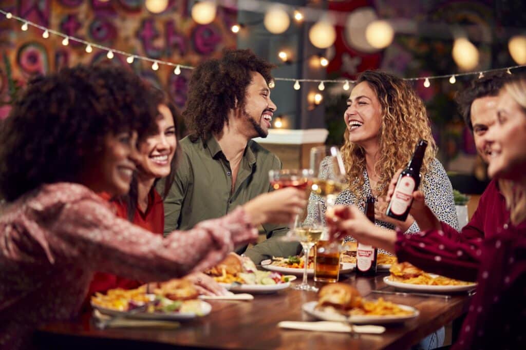 Multi-Cultural Group Of Friends Enjoying Night Out Eating Meal And Drinking In Restaurant Together