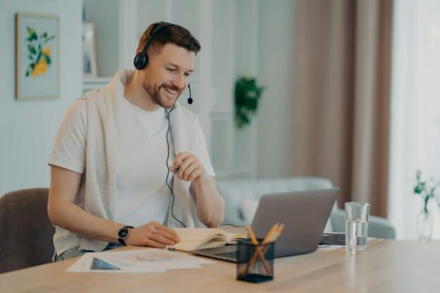 Happy man enjoying learning at home and using headset and laptop